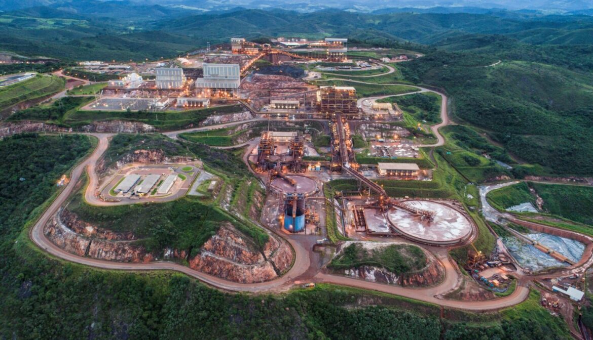 Estrutura de mineração com galpões, tanques e vias internas em área verde montanhosa