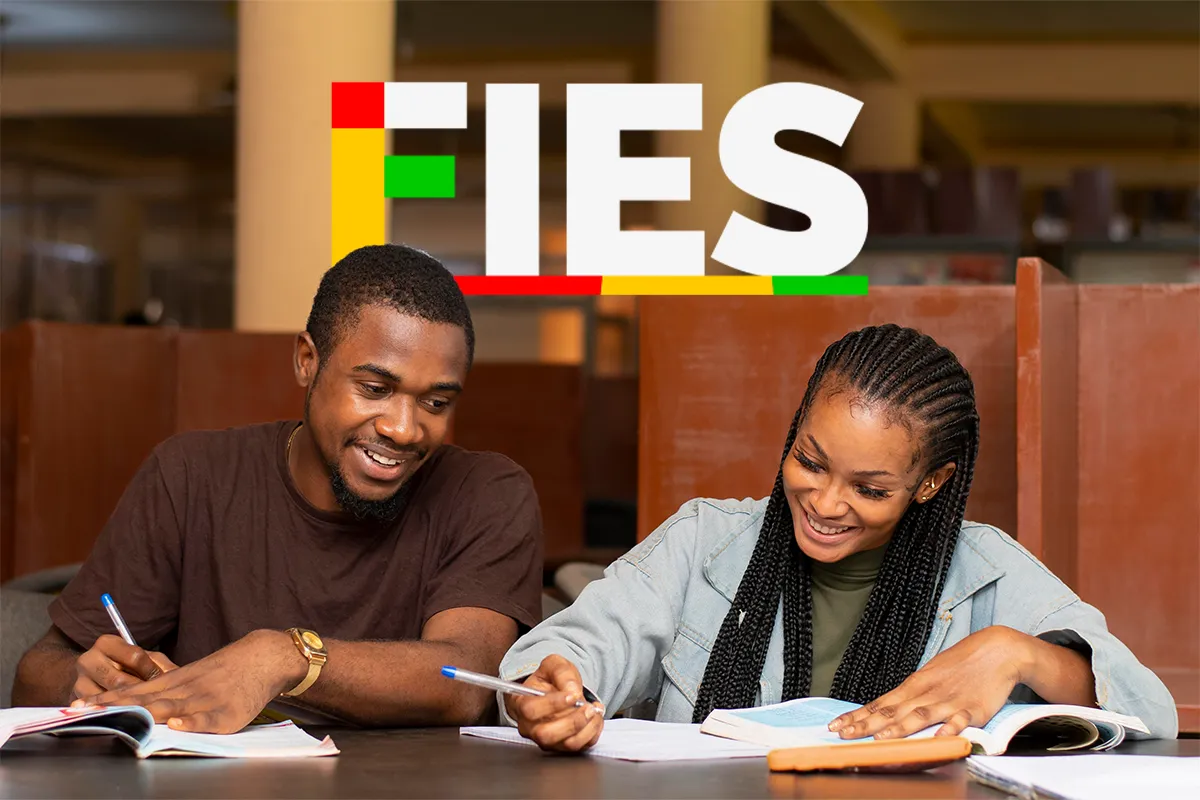 Fies: pré-selecionados devem complementar inscrição até amanhã, 24 6 Dois jovens escrevendo em cadernos abertos, sorrindo em ambiente de estudo com logo do Fies ao fundo