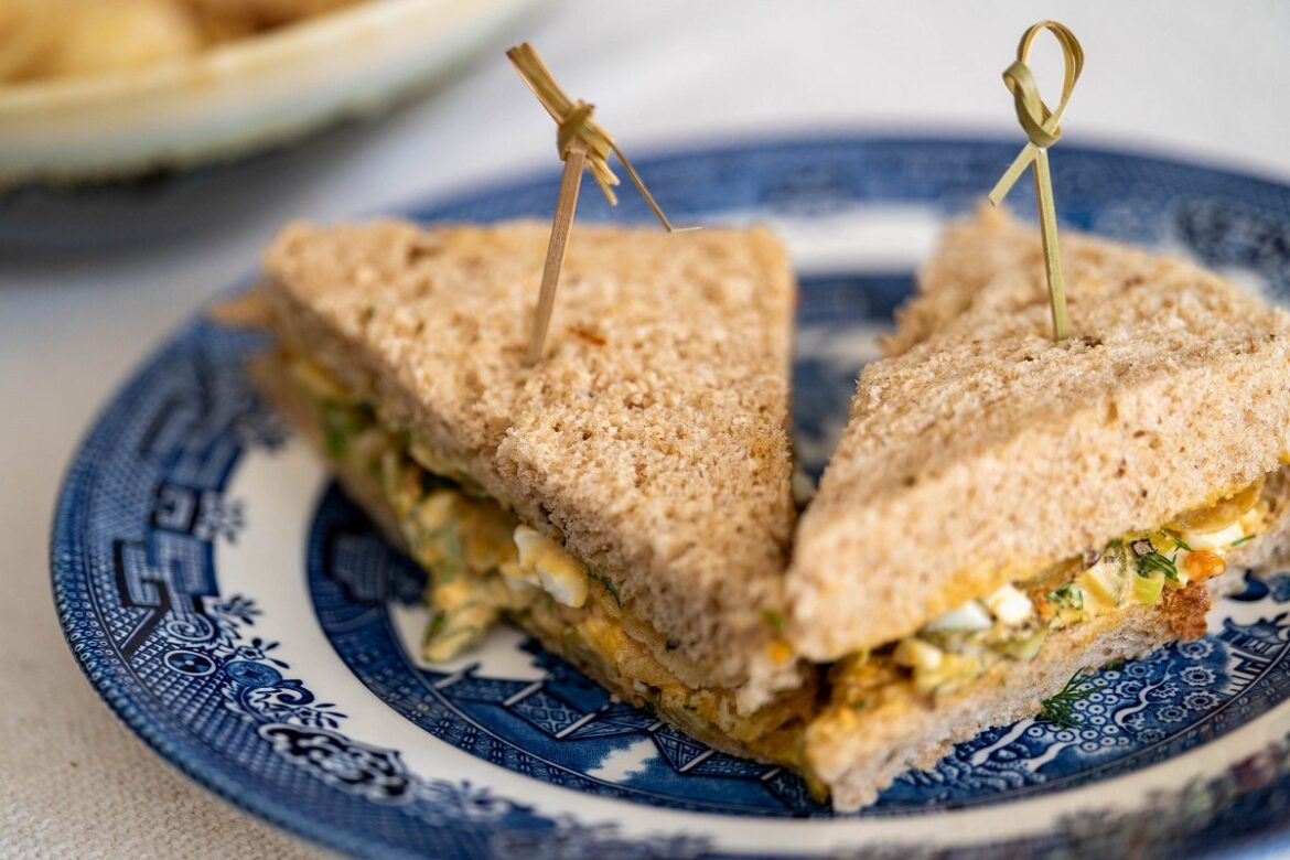 Dois sanduíches de pão integral cortados ao meio recheados com ovo cremoso em prato decorado