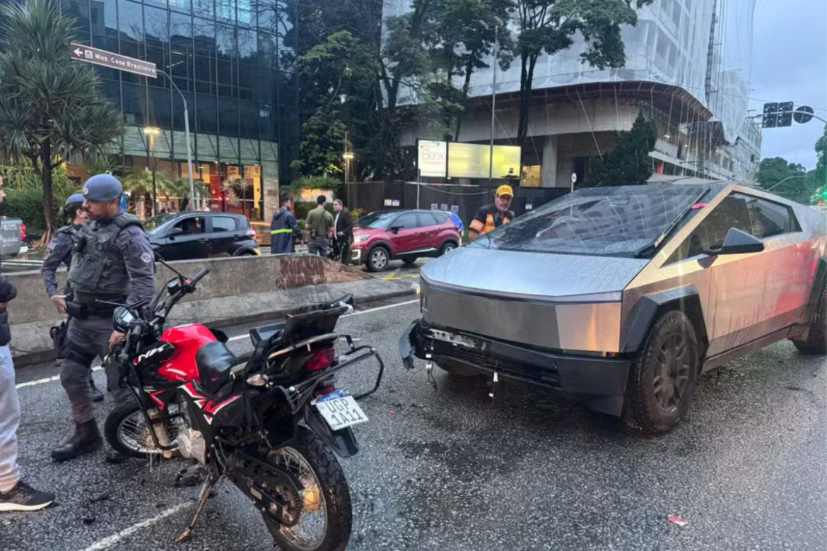 Policiais observam moto danificada ao lado de Tesla Cybertruck parada em avenida molhada
