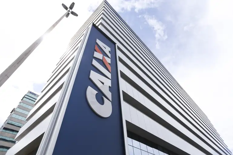 Faça parte da CAIXA: processo seletivo para estágio oferece vagas; saiba como se inscrever 6 Prédio da CAIXA com letreiro azul em destaque sob céu claro, visto de baixo para cima