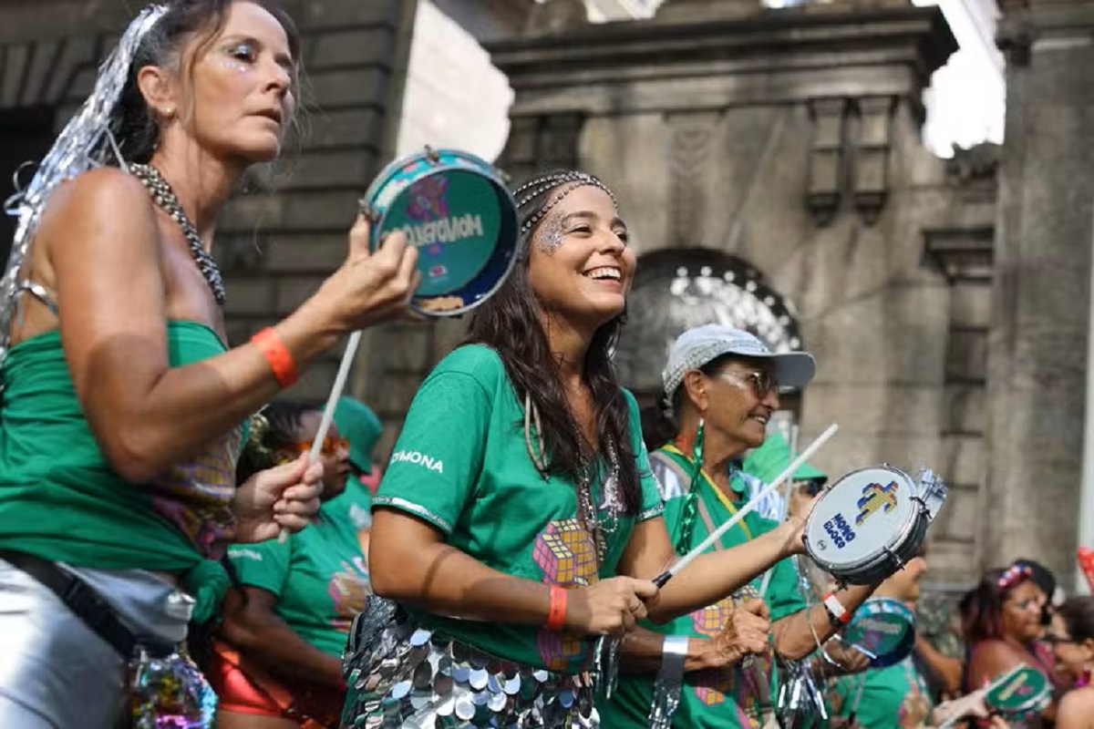 Contagem regressiva para o Carnaval 2026: Tendências, blocos e o que não pode faltar na sua folia 6 Grupo de mulheres com fantasias verdes tocando tamborim e sorrindo durante bloco de Carnaval