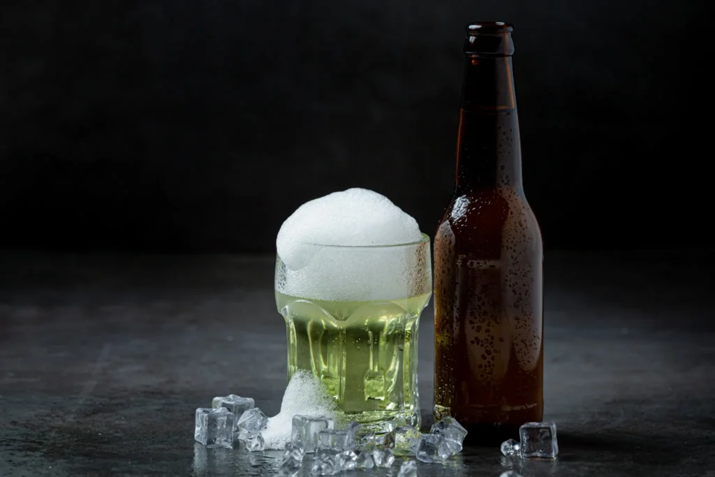 Envolva a garrafa de cerveja ou refrigerante dessa forma para ela gelar em apenas 5 minutos 6 Garrafa de cerveja e copo com espuma, acompanhados de cubos de gelo sobre uma superfície escura.