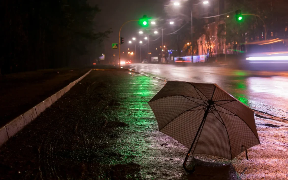 Guarda-chuva em calçada molhada durante chuva noturna com previsão de temporais em várias regiões do Brasil.