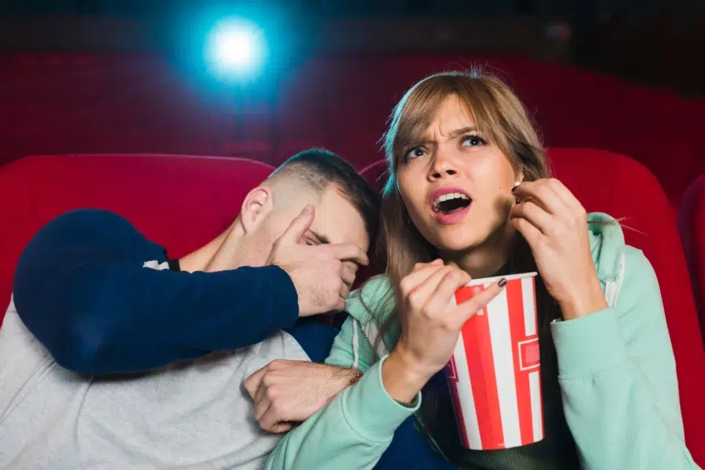Nova lei garante sessões de cinema adaptadas para pessoas com autismo 6 Casal assistindo a um filme em um cinema, com expressão de surpresa e desconforto.