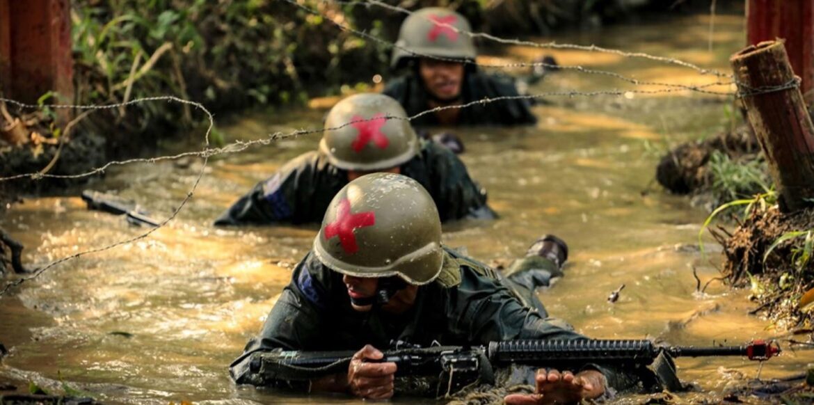 Fuzileiros Navais em treinamento militar rastejando na água sob arame farpado