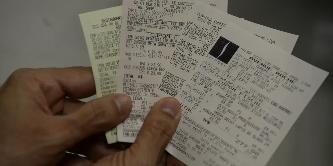 Mão adulta segurando vários cupons fiscais impressos próximos uns dos outros