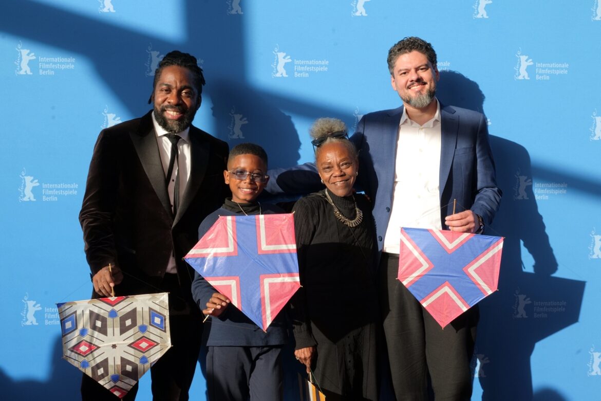 Quatro pessoas sorrindo exibem pipas coloridas diante de painel do Festival de Berlim