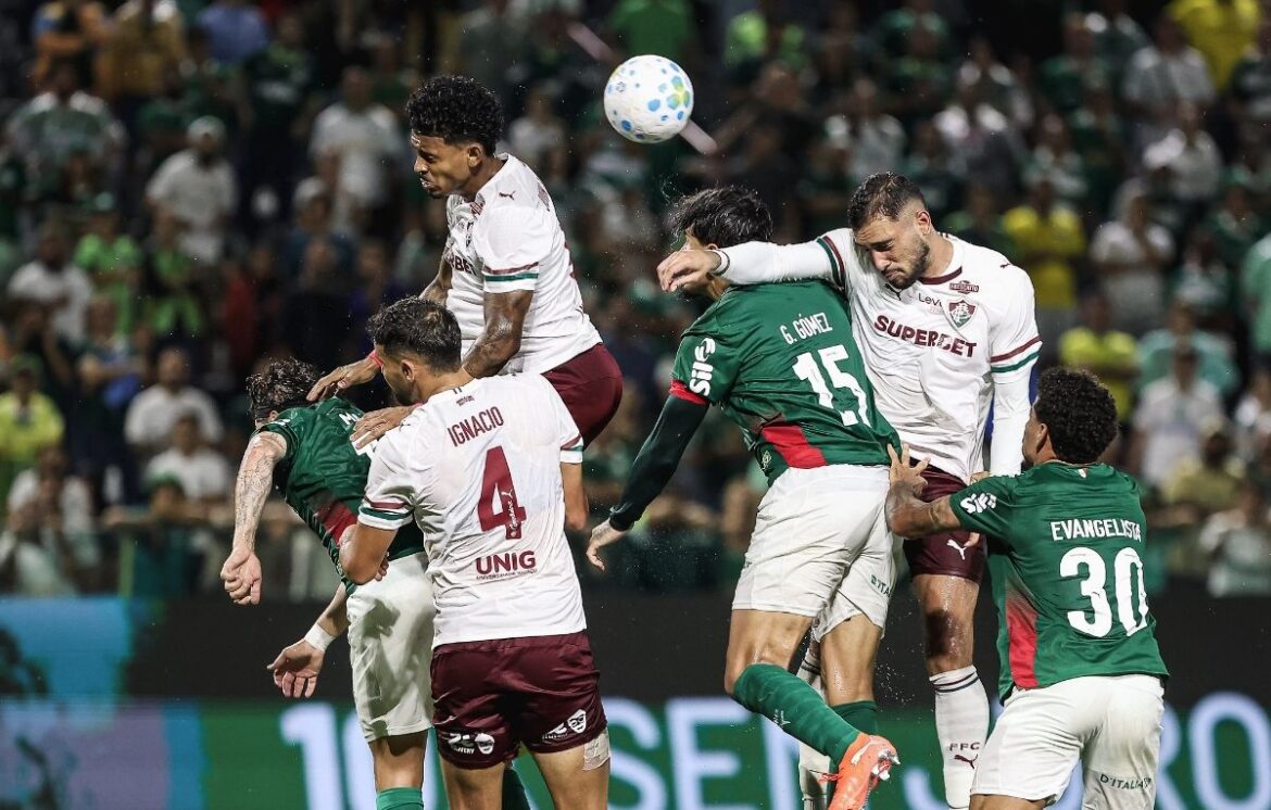 Jogadores de times rivais saltando juntos para cabecear a bola durante partida intensa