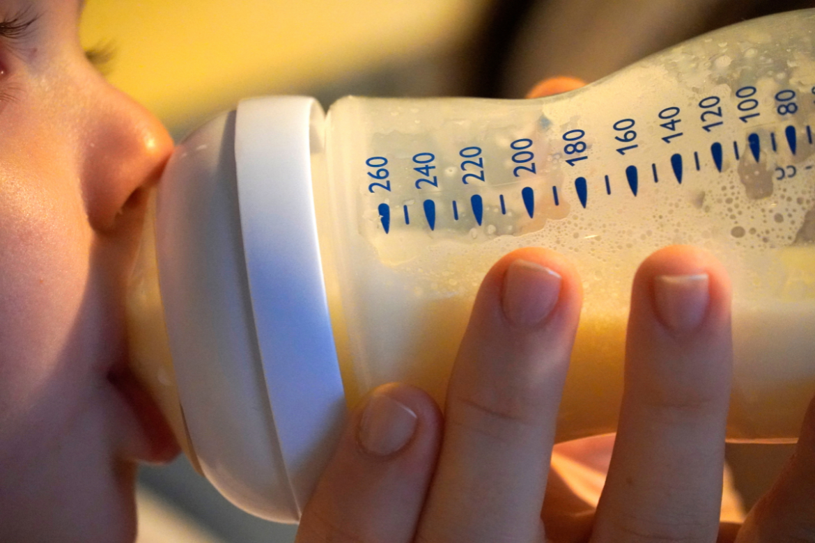 Bebê bebe leite em mamadeira enquanto segura o recipiente com as mãos