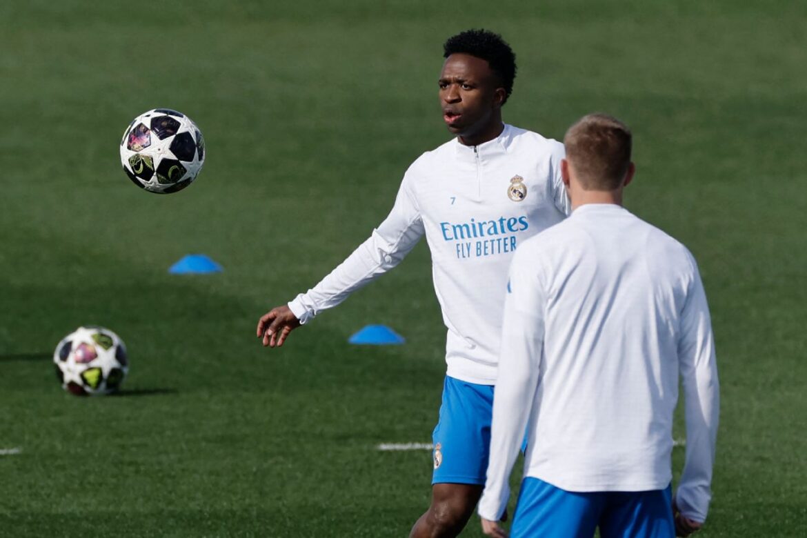 Atleta do Real Madrid observa bola no ar durante treino com companheiro em campo