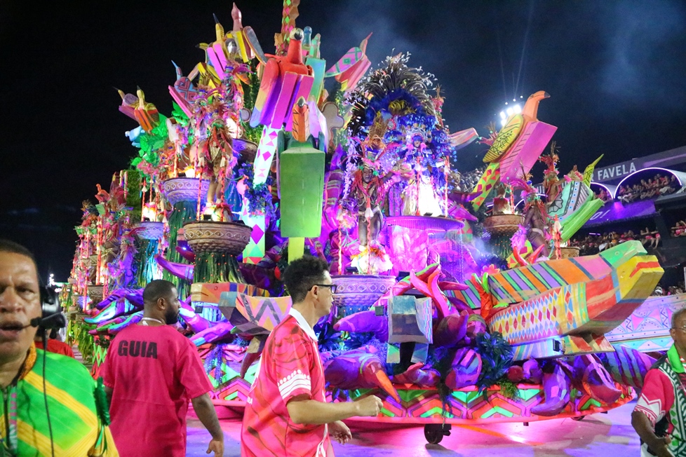 Carnaval do Rio 2026: apuração das notas e anúncio da campeã ocorrem nesta quarta 6 Carro alegórico monumental da Mangueira no Carnaval 2026, apresentando cores vibrantes como rosa, verde, amarelo e azul. A alegoria possui esculturas de pássaros tropicais, componentes fantasiados em diversos níveis e iluminação cênica intensa sob o céu noturno da Sapucaí.