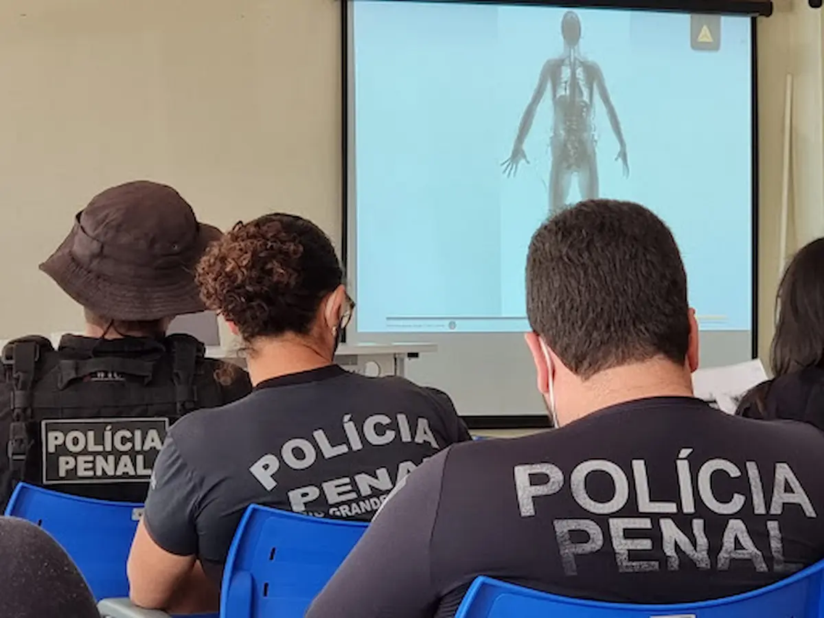 Concurso Polícia Penal do RN: edital será publicado em março, anuncia governo 6 Três agentes da Polícia Penal do Rio Grande do Norte assistindo a uma palestra técnica. Dois vestem camisas pretas com a inscrição "POLÍCIA PENAL" e um utiliza colete tático e chapéu de selva.