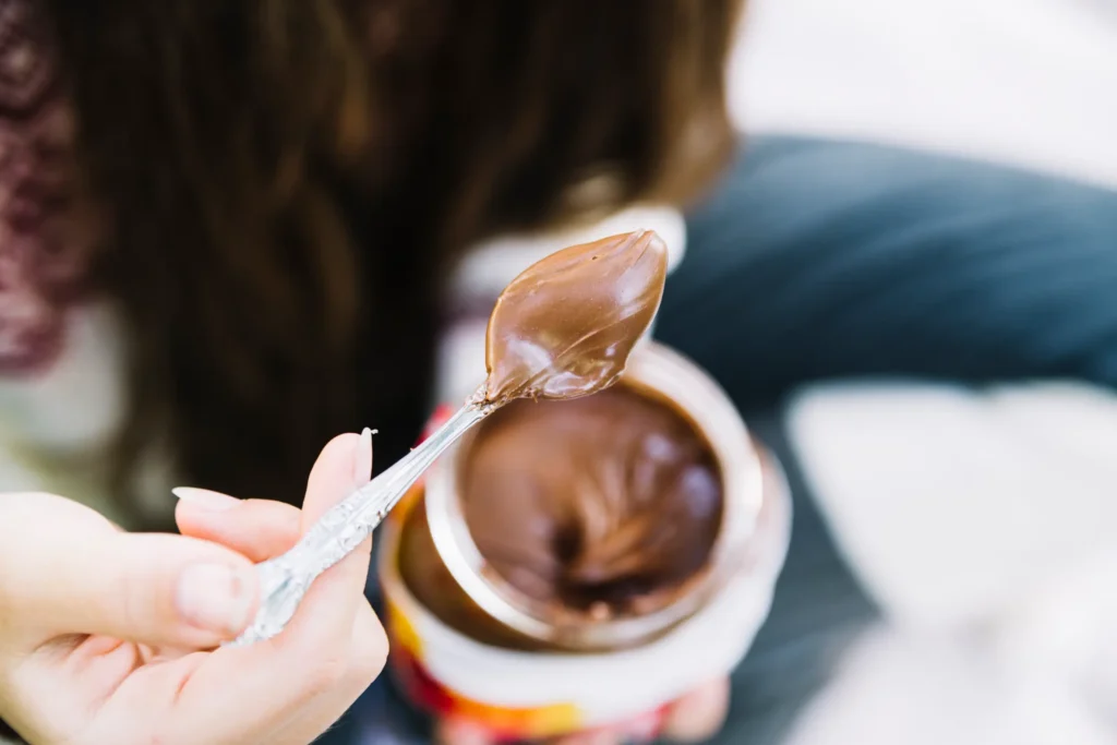 Doce problema: Nutella quase causa exclusão de italiana nas Olimpíadas de Inverno 6 Uma colher de Nutella com uma camada cremosa, capturada por uma mão, próximo ao pote de Nutella.