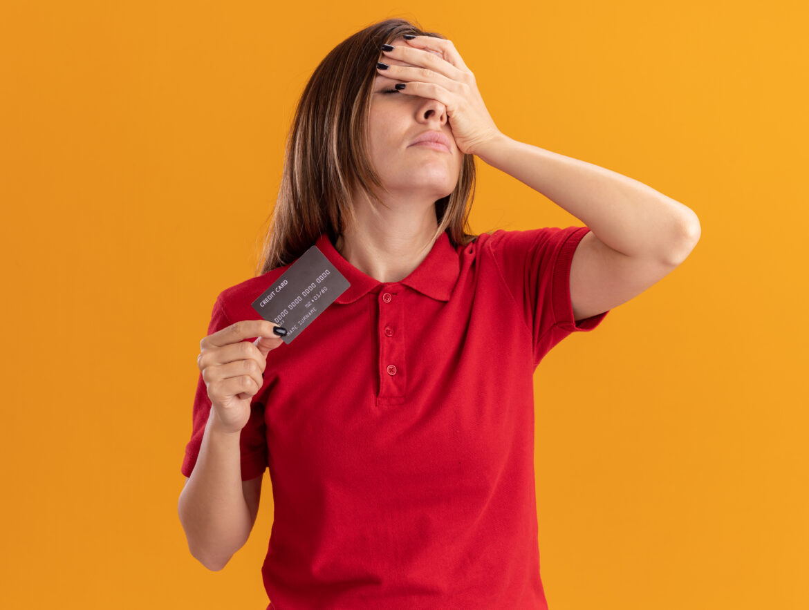 Mão segurando cartão de crédito ao lado de relógio sobre mesa