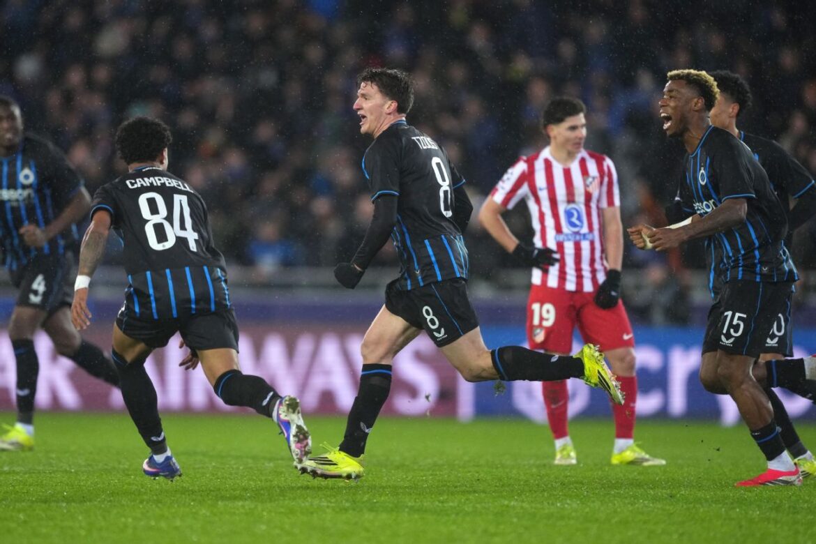 Atletas de uniforme preto comemoram gol enquanto adversário em vermelho observa desanimado no gramado