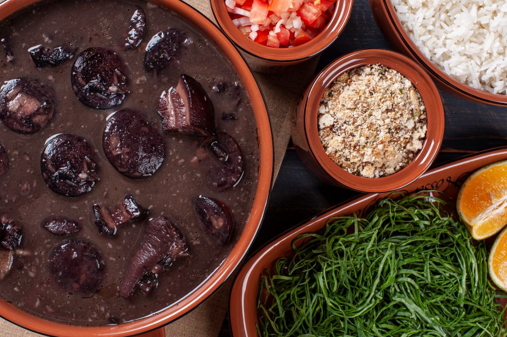 Como fazer uma feijoada tradicional: deliciosa e com gostinho de "quero mais" 6 Close-up de uma panela de barro marrom com feijão preto, rodelas de linguiça calabresa, pedaços de lombo e bacon imersos em um caldo de feijão encorpado e brilhante.
