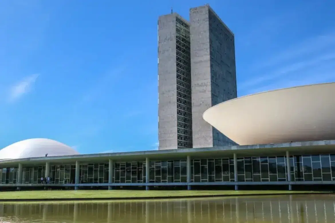 Vista do Congresso Nacional em Brasília com as torres gêmeas e as cúpulas do Senado e da Câmara refletidas no espelho d’água.