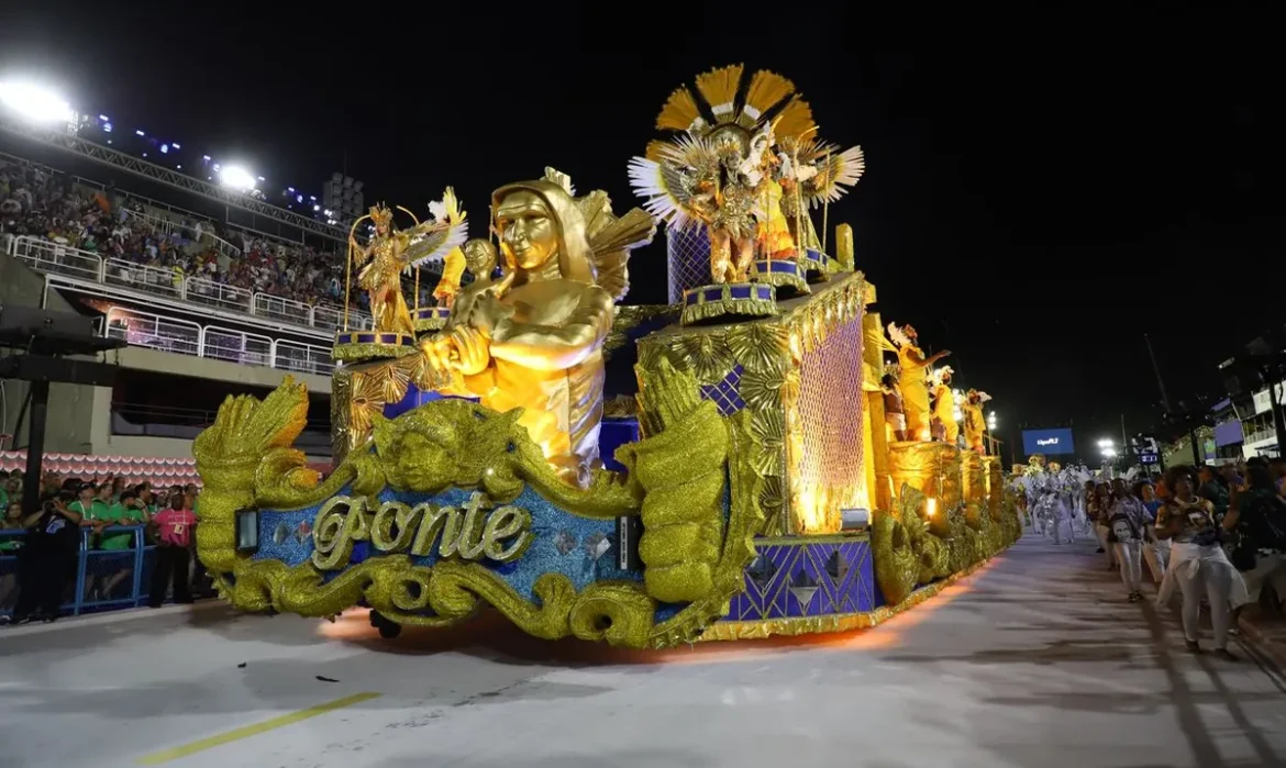 Carro alegórico dourado da Série Ouro desfila na Marquês de Sapucaí com arquibancadas lotadas à noite.