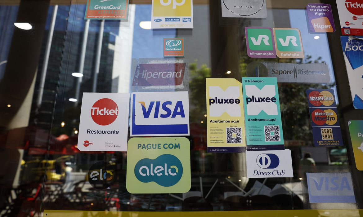 Novas regras para vale-refeição e alimentação atingem empresas antes protegidas; saiba mais 6 Diversos adesivos de cartões refeição, alimentação e crédito em janela de restaurante