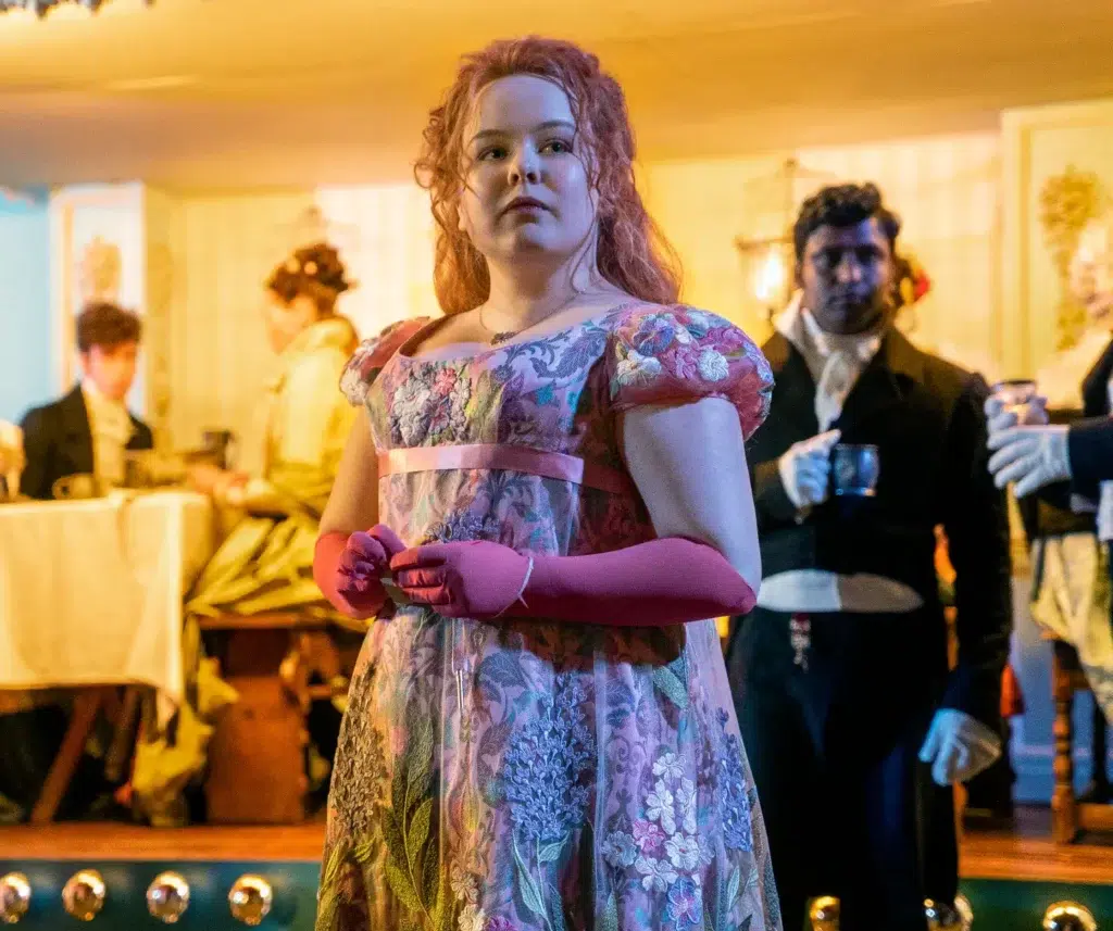 5ª temporada de Bridgerton: data de estreia, nova protagonista e Lady Whistledown - veja o que já se sabe 6 Personagem de Bridgerton com vestido floral e luvas rosas em salão de baile da série da Netflix, em cena que antecede a aguardada 5ª temporada
