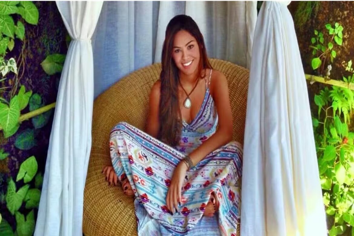 Gabriela sorridente em cadeira de vime em varanda cercada por plantas.