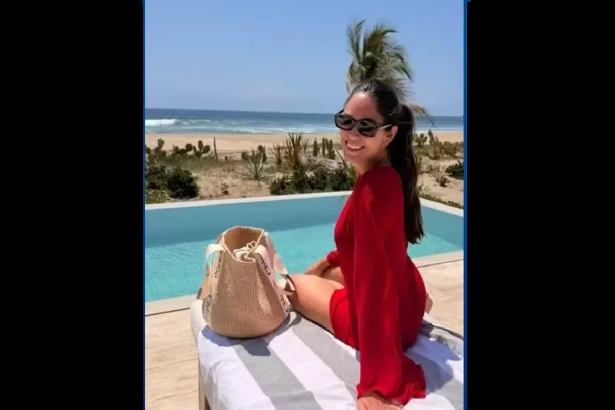 Advogada brasileira de 31 anos morre afogada em praia do México durante viagem de férias 6 Gabriela sorridente sentada de vestido vermelho ao lado de piscina, com bolsa de palha e mar ao fundo