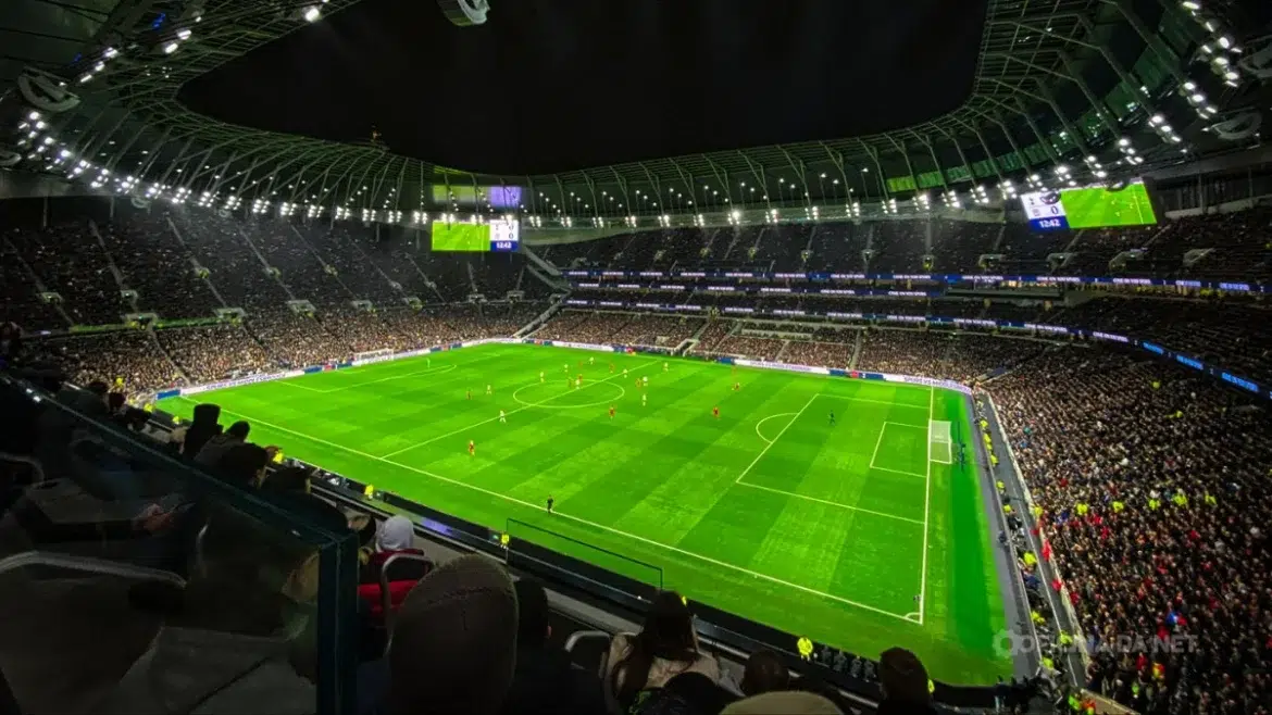 Torcedores assistindo a jogo de futebol com estádio cheio sob luzes intensas à noite