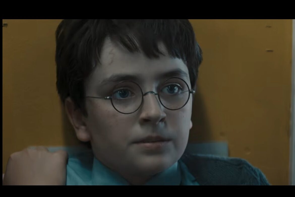 Harry Potter de cabelos escuros usando óculos redondos encara algo em ambiente iluminado