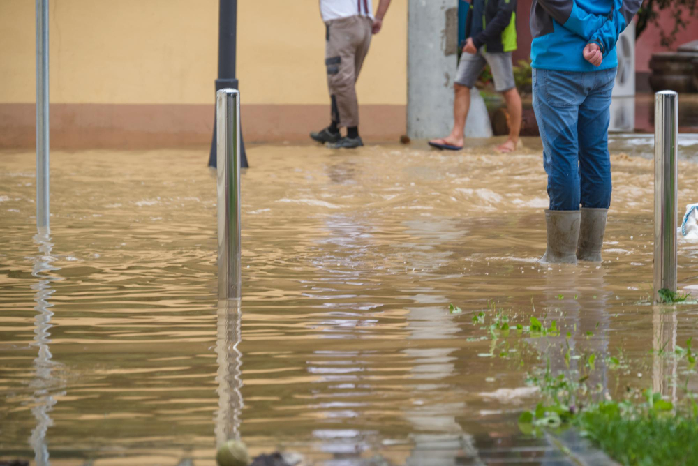 Previsão do tempo: fim de semana com temporais, chuvas fortes e muito calor 6 Moradores caminham em rua inundada, alguns com botas, durante enchente causada por chuvas fortes