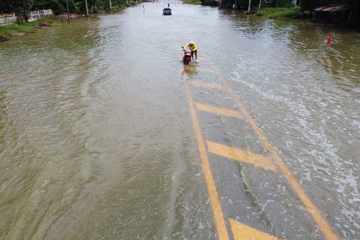 Homem empurrando moto em via tomada pela água após chuva intensa