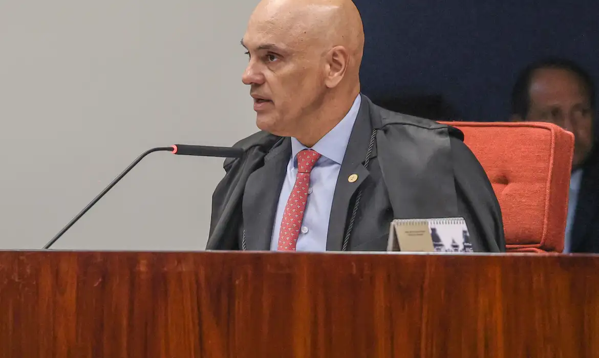 Qual a relação entre Alexandre de Moraes a Daniel Vorcaro? Veja o que se sabe até agora 6 Homem careca de toga preta e gravata vermelha sentado em mesa de madeira diante de microfone