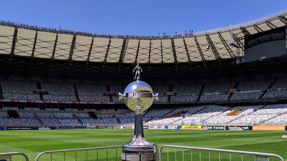 Troféu da Copa Libertadores exposto no gramado de estádio vazio iluminado pelo sol