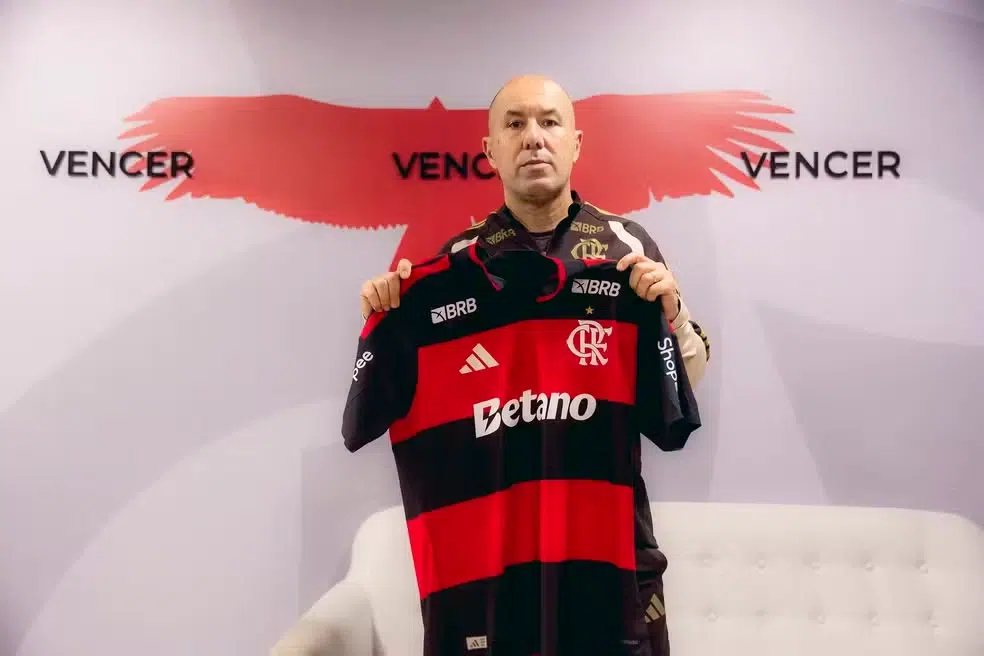 Flamengo adota nova estratégia de gestão: Jardim assume para evitar crise imediata 6 Homem calvo veste agasalho do Flamengo e segura camisa oficial diante da parede com urubu e palavras “vencer”