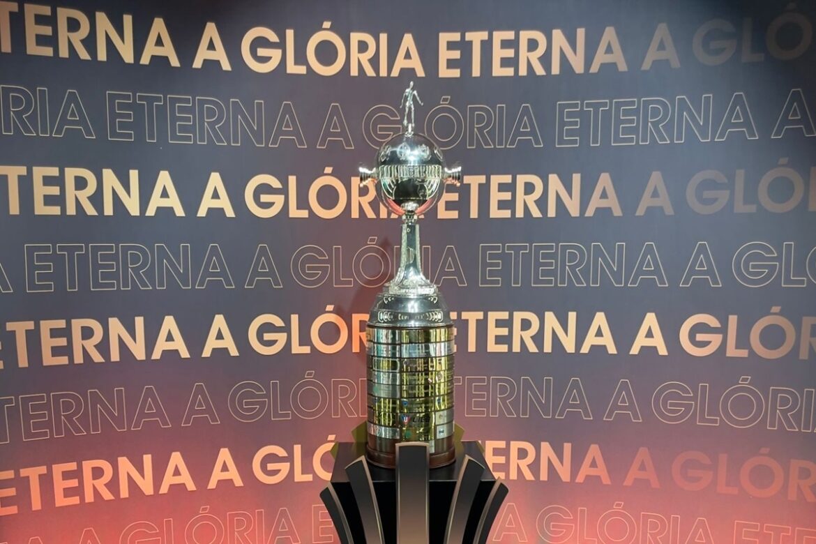 Troféu da Libertadores posicionado em frente a painel com a frase “A Glória Eterna”