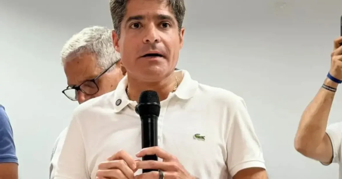 Homem segurando microfone durante coletiva de imprensa, com expressão séria