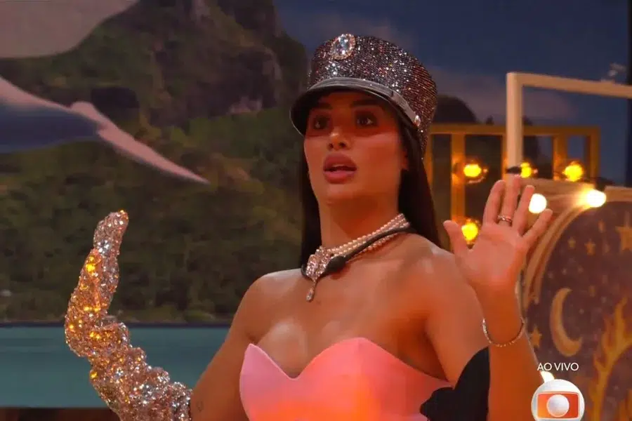BBB 26: veja o resumo da madrugada com retorno do Quarto Secreto, mal-estar de Marciele e choro de Jonas 6 Mulher com chapéu brilhante e luva prateada ergue as mãos em expressão de surpresa no cenário do BBB 26