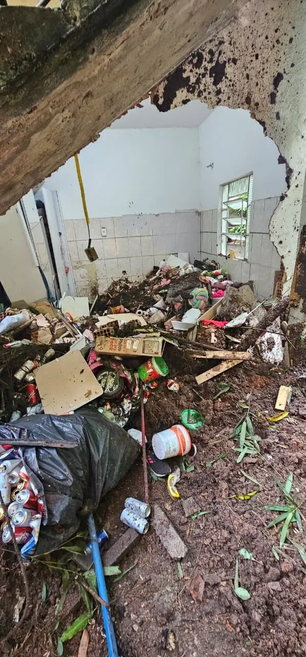 Governo antecipa Abono Salarial e libera parcelas extras do Seguro-Desemprego em municípios atingidos por chuvas 6 Interior de uma residência destruída por deslizamento de terra em Juiz de Fora; uma parede quebrada revela entulhos, lama e objetos domésticos soterrados.