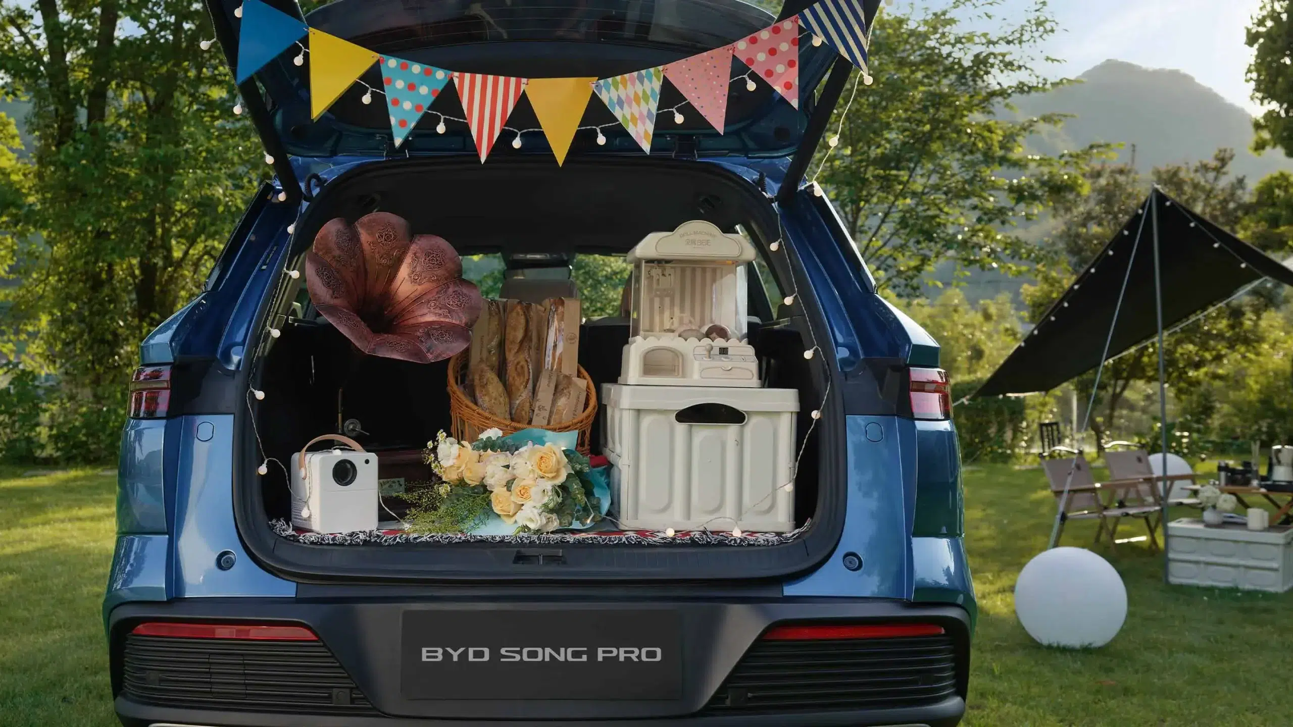BYD Song Pro lança versão híbrida que percorre 301 km sem usar gasolina 6 Traseira do BYD Song Pro azul com porta-malas aberto exibindo gramofone, flores, projetor e caixas em cenário de camping