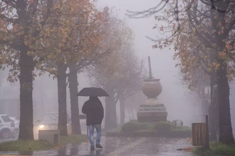 Calor intenso em parte do Brasil, mas chuva e frio também chegam, aponta Inmet 6 Pessoa caminha sob guarda-chuva preto em praça com neblina densa, placa de São Francisco de Paula ao fundo