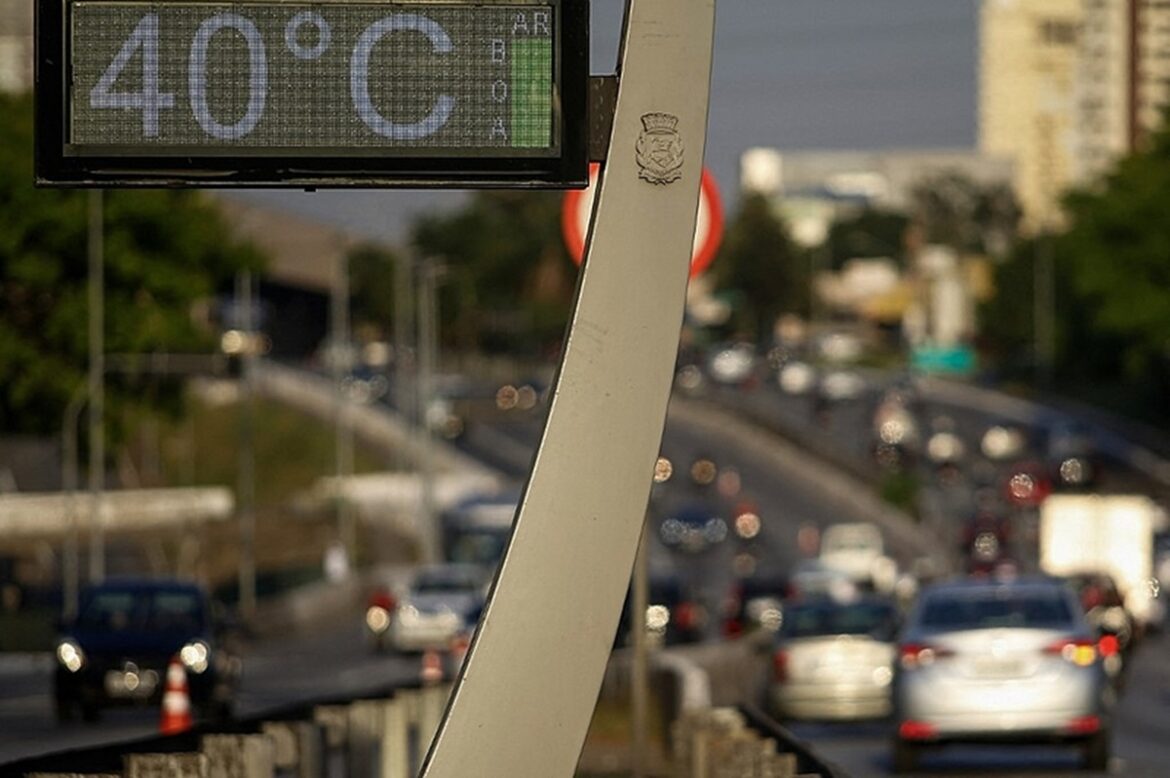 Termômetro digital em poste exibe 40°C com emblema municipal, tráfego de carros desfocado ao fundo em avenida paulistana
