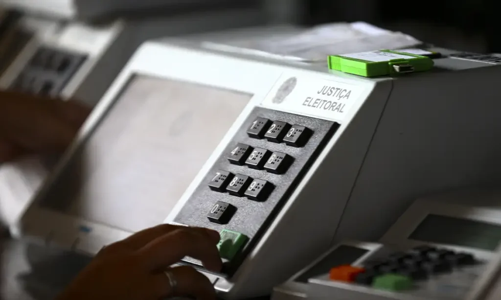 Tire e regularize seu título de eleitor até 6 de maio para votar nas eleições 2026 6 Eleitor digitando voto em urna eletrônica durante processo de votação das eleições gerais de 2026.