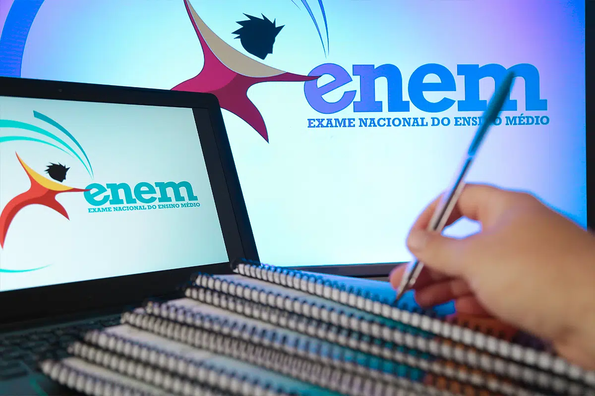 Isenção Enem 2026: prazo para solicitar gratuidade na taxa de inscrição vai até 24 de abril 6 Estudante escreve em caderno com caneta enquanto notebook exibe logo do Enem ao lado de tela maior com marca do exame