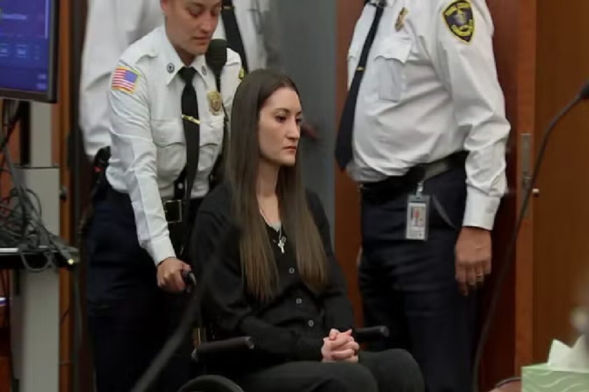 Lindsay Clancy sentada em cadeira de rodas vestindo roupa preta no tribunal ao lado de oficiais