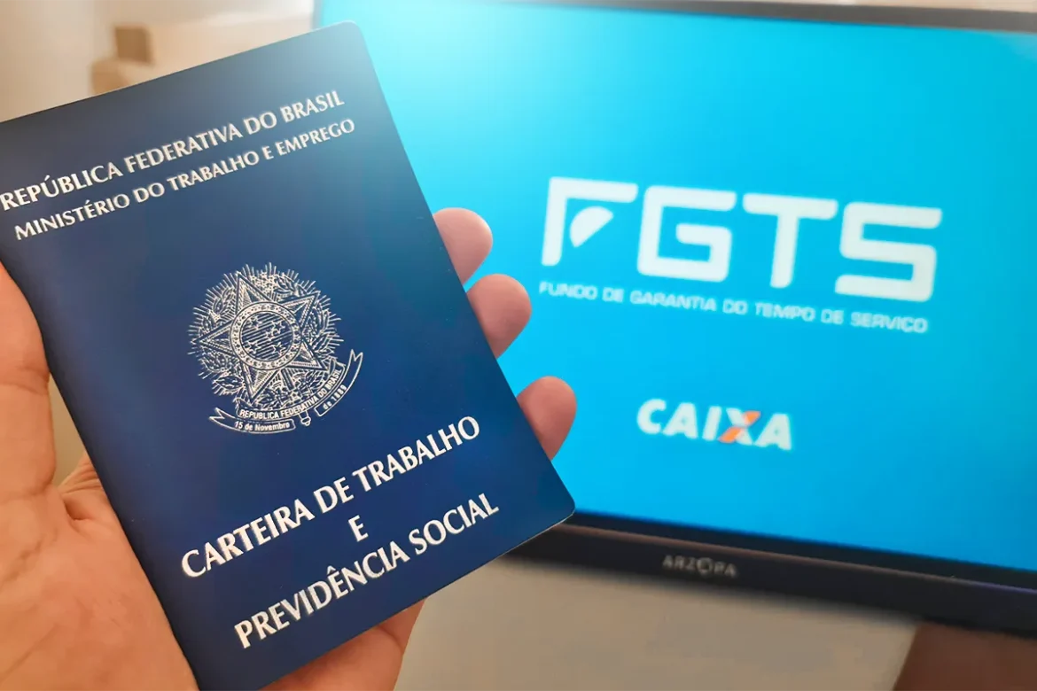 Mão segura Carteira de Trabalho azul com brasão do Brasil, ao fundo monitor exibe logo FGTS e Caixa em tela azul