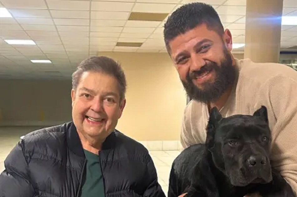 Faustão volta a aparecer nas redes e apresenta seu novo cachorro 6 Faustão sorridente ao lado de Victor Gabriel Marques segurando um cachorro Cane Corso preto em ambiente interno