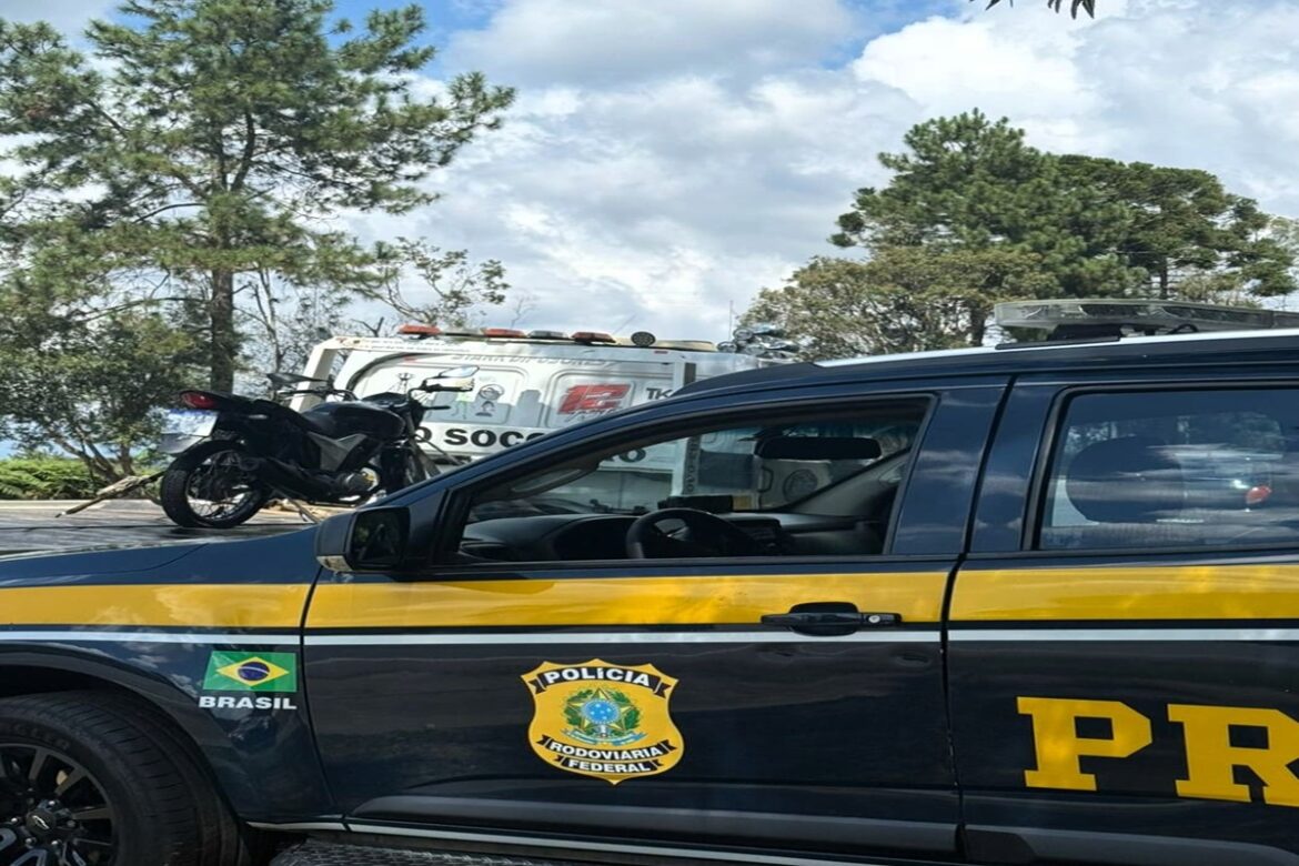 Viatura da PRF com brasão e faixa amarela em primeiro plano, moto preta apreendida sobre guincho ao fundo