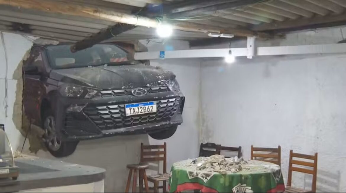 Carro Hyundai cinza com placa TXJ2B62 atravessa parede de bar, com mesas e escombros visíveis ao redor
