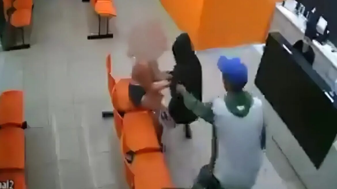 Mulher sentada em cadeira laranja se defende de homem de preto enquanto outro homem de boné azul se aproxima