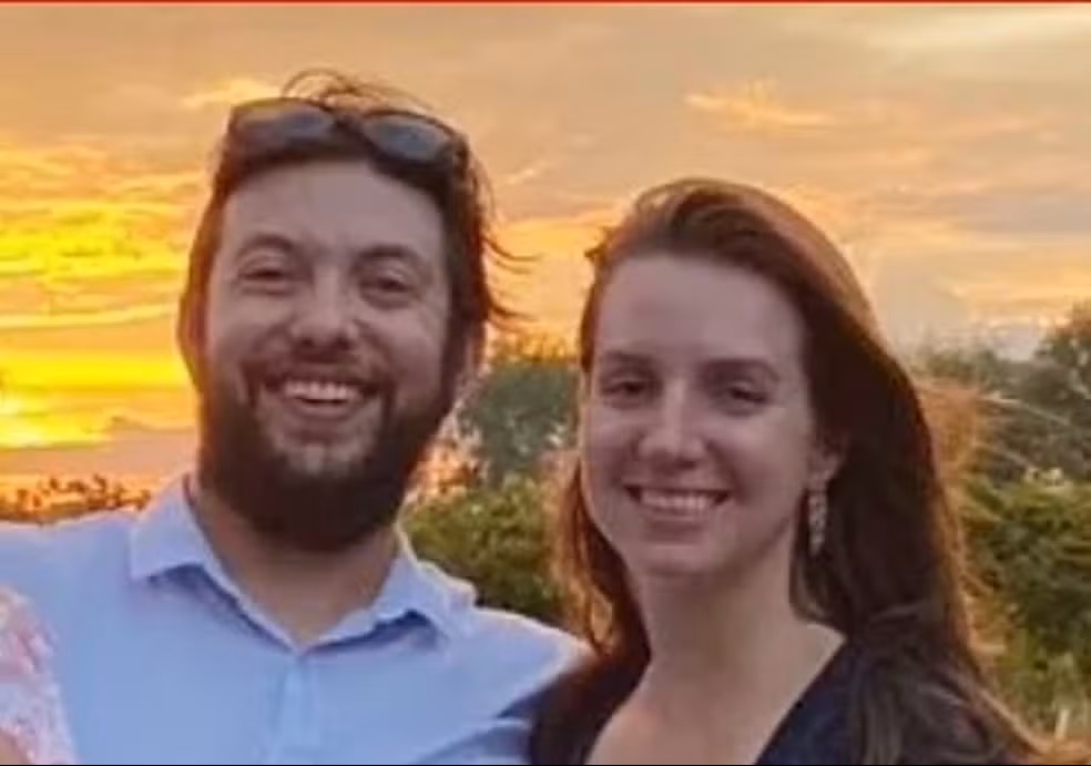 Mulher usa 'massagem sensual' para matar o pai dos seus filhos em subúrbio de Chicago 6 Casal sorri ao pôr do sol; homem de barba, camisa azul e óculos na cabeça, mulher de cabelo castanho e blusa preta